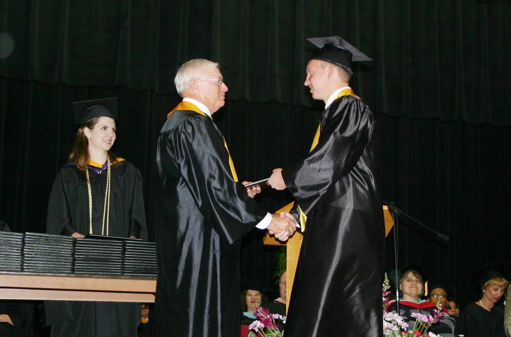 Click to enlarge,  William Gaschler IV, of Sanford, (right) receives his Associate in Applied Science degree from Bobby Powell, chairman of the Central Carolina Community College Board of Trustees, during the college&#8217;s Summer Commencement exercises Friday in the Dennis A. Wicker Civic Center. Assisting in handing out the degrees, diplomas and certificates was Jessica Brown (back, left), the college&#8217;s Instructor of the Year and a semifinalist for the North Carolina Community College System&#8217;s Excellence in Teaching Award. During the summer, 89 students completed degrees, 102 earned diplomas, and 84, certificates. Teddy Byrd, chairman of the Harnett County Board of Commissioners delivered the commencement address.  