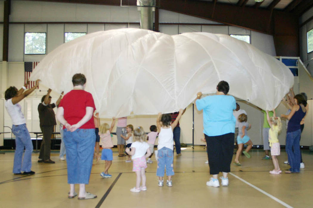 Click to enlarge,  Children participating in the Stevens Center&#8217;s Party, Paint and Playtime summer camp enjoy running under a billowing parachute held by members of Central Carolina Community College&#8217;s early childhood education program and nursing students from UNC-Chapel Hill. The community college and university students collaborated to staff and plan activities for the Center&#8217;s summer camp for 2-to-4-year-olds and its Kids Can Connect camp for 5-to-8-year-olds, held during June and July. Both camps included children with and without disabilities. The nursing students gained experience working in the community and the CCCC students applied what they had learned in class about working with young children with and without disabilities, individually and in groups.  