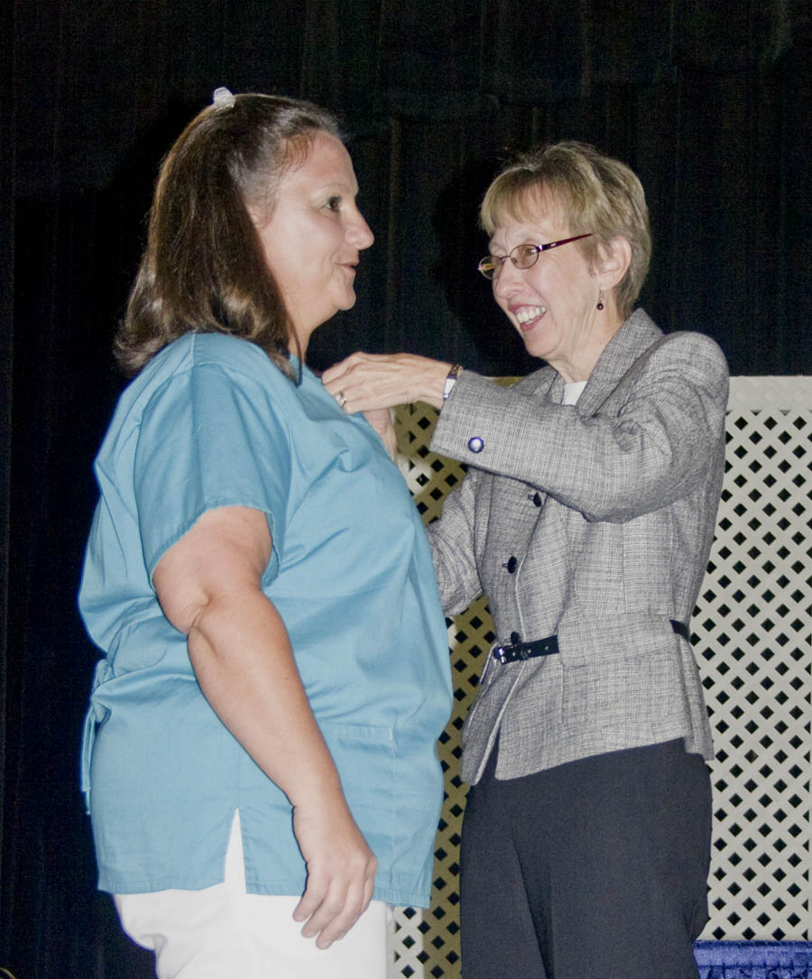 Click to enlarge,  Judy Farmer (right), CCCC Continuing Education Health Program Coordinator in Lee County, attaches a nursing pin to the blouse of Shanna Moore, of Harnett County. Shanna received her Nursing Assistant II certificate at the Central Carolina Community College Lee County Continuing Education Department&#8217;s Medical Programs Graduation May 27 at the Dennis A. Wicker Civic Center.&amp;nbsp; 