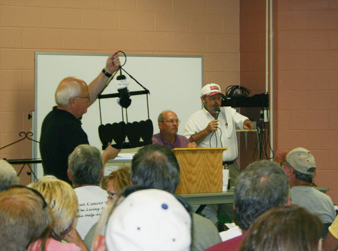 Click to enlarge,  Bill Tyson (left), Harnett provost for Central Carolina Community College, hoists a plant holder for bidders to see during the CCCC Foundation&#8217;s Furniture Auction June 6. Keeping track of the bids is Ed Taylor (center), instructor in the college&#8217;s carpentry program at Harnett Correctional Institution, while auctioneer R.J. Wicker (right), of Sanford, acknowledges a bid. The auction, at the college&#8217;s Harnett County Campus in Lillington, attracted more than 100 people. A variety of wood and metal furnishings were auctioned for a total of more than $19,000. Student inmates of the college&#8217;s carpentry and welding programs in the Harnett Correctional Institution made all the pieces. Proceeds from the annual auction go into an endowment that provides scholarships for Central Carolina students from Harnett County. 