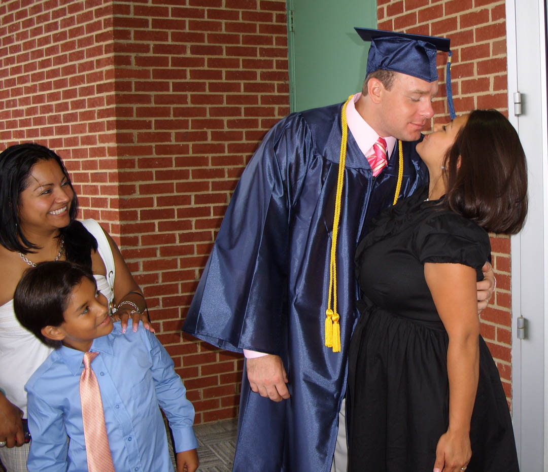 Click to enlarge,  Central Carolina Community College Adult High School graduate Bryan Reynolds (center) gets a congratulatory kiss from his wife, Indira, as their son, Jaffet, and friend Iris Alduvin watch.&amp;nbsp; Reynolds graduated with a straight-A grade point average. He was the Lee County student speaker at the college&#8217;s June 18 Adult High School and General Educational Development graduation at the Dennis A. Wicker Civic Center. Reynolds now plans to enlist in the U.S. Army and become a combat medic. Approximately 190 adults completed high school or a GED through the college&#8217;s adult education program during the spring semester.&amp;nbsp; 