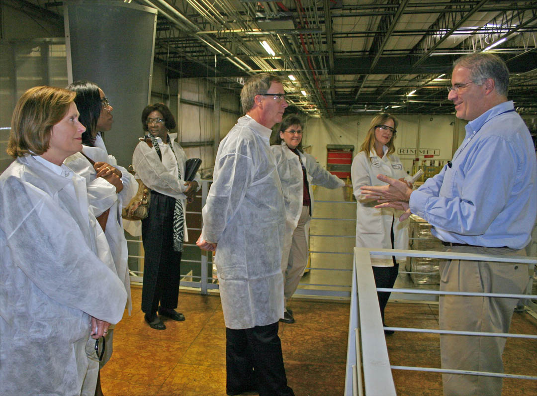 Click to enlarge,  Joe Lascala (right), director of Logistics at Coty Inc.&#8217;s Sanford plant, describes the company&#8217;s product distribution system for visitors from Central Carolina Community College. The college&#8217;s Industry Services office recently received $174,046 in funding from the North Carolina Community College System&#8217;s Customized Training Program for workforce training at the Broadway Road plant. Pictured (from left) wearing company required white &#8216;clean&#8217; jackets for the Nov. 8 tour of the million-square-foot plant are Diane Glover, executive director of the CCCC Foundation; Stelfanie Williams, vice president for the college&#8217;s Economic and Community Development Division; Phyllis Huff, dean of Adult and Continuing Education; college President Bud Marchant; Cathy Swindell, CCCC Industry Services officer; and Katy Caselli, Coty&#8217;s Human Resources Learning and Development manager at the plant. Stephen Athans, dean of the college&#8217;s Vocational and Technical Programs was also on the tour. 