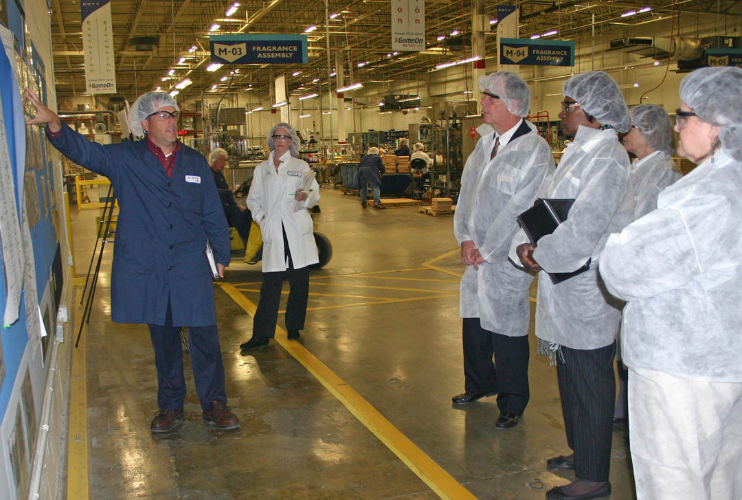 Click to enlarge,  Tim Hughes (left), director of Ops and Strategy Improvement at Coty Inc.&#8217;s Sanford plant, explains the company&#8217;s Plan-Do-Check work board to visitors from Central Carolina Community College during a Nov. 8 tour of the plant. The college&#8217;s Industry Services office recently received $174,046 in funding from the North Carolina Community College System&#8217;s Customized Training Program for workforce training at the Broadway Road plant. Pictured (from second left) wearing company required white &#8216;clean&#8217; jackets for the tour of the million-square-foot plant are Katy Caselli, Coty&#8217;s Human Resources Learning and Development manager at the plant; college President Bud Marchant; Phyllis Huff, dean of Adult and Continuing Education; Diane Glover, executive director of the CCCC Foundation; and Cathy Swindell, CCCC Industry Services officer. Also on the tour were Stelfanie Williams, vice president for the college&#8217;s Economic and Community Development Division and Stephen Athans, dean of the college&#8217;s Vocational and Technical Programs. 