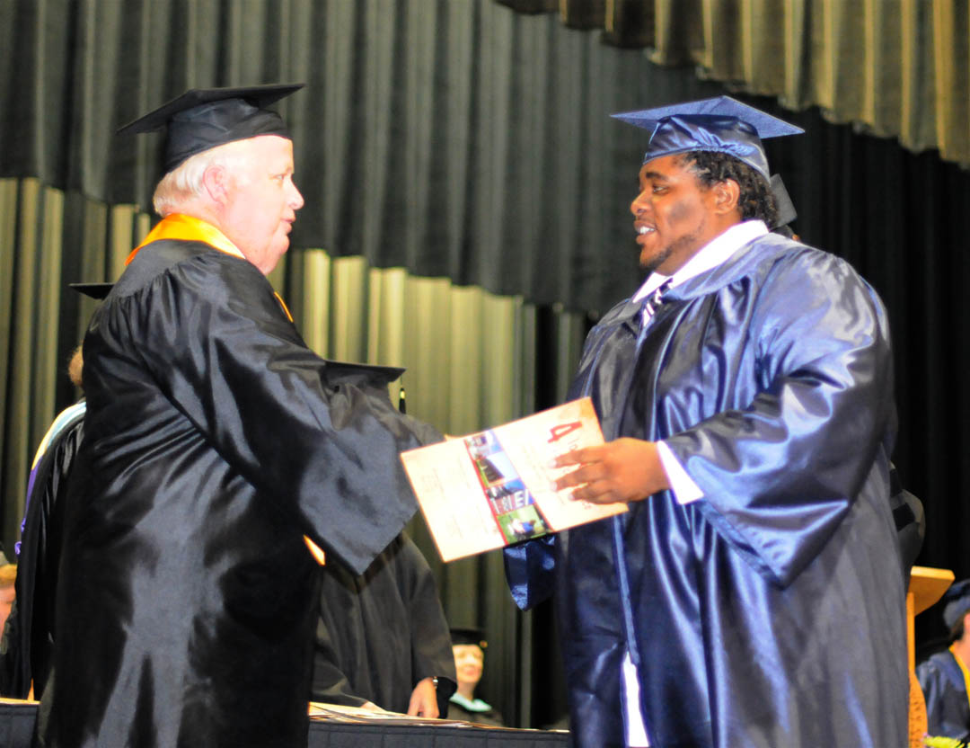 Click to enlarge,  Ed Garrison, chairman of the Central Carolina Community College Board of Trustees, congratulates graduating student Victor Bass, of Harnett County, after presenting him with the W.B. Wicker Memorial Scholarship at the college&#8217;s June 16 Adult High School/GED graduation exercises. Bass was also one of three graduating student speakers. He plans to continue his education at the college in the Computer Engineering Technology program. A total of 143 students completed their AHS or GED studies during the spring semester.&amp;nbsp; 