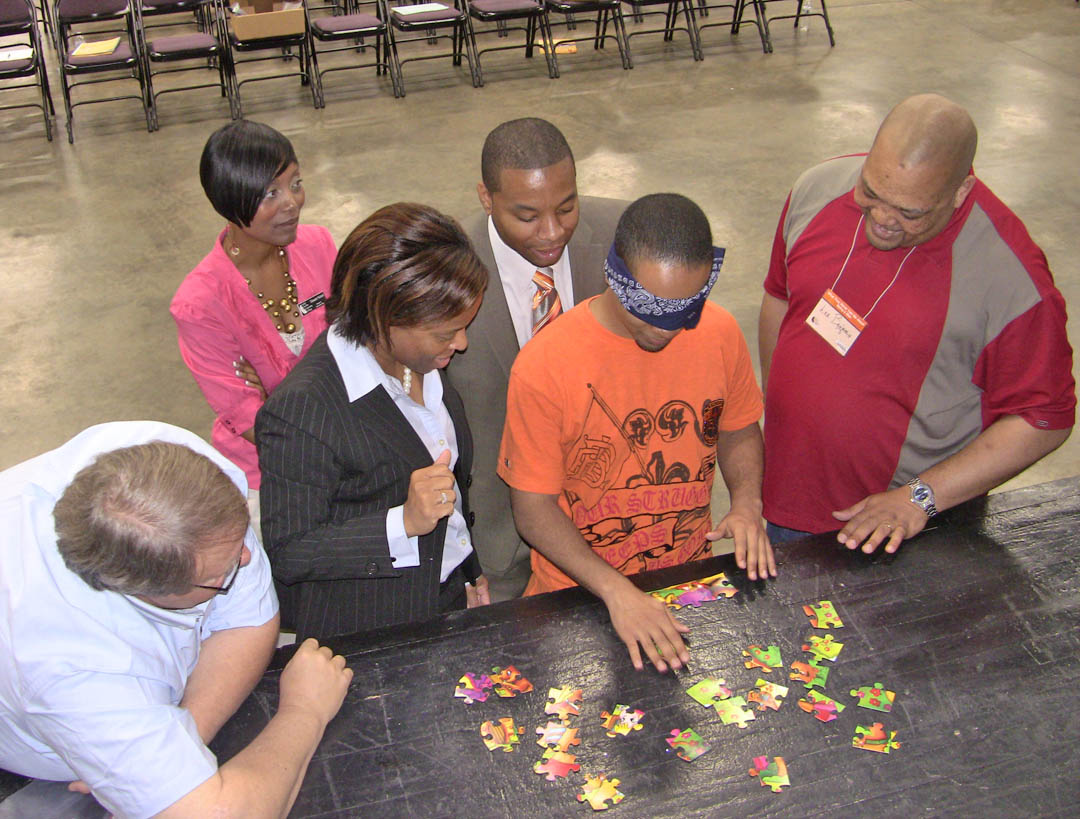 Click to enlarge,  Learning to follow directions and teamwork - even when blindfolded - was one of the fun learning activities at the 'What They Never Told Me About Being a Man' event held March 23 at the Dennis A. Wicker Civic Center. From left, Tim Eyring, Central Carolina Community College  Admissions Counselor; Trinnette Nichols, CCCC director of Student Services; Dawn Tucker, CCCC dean of College and Career Readiness; Tawan Perry, one of the event motivational speakers, and CCCC student Lee Benjamin offer encouragement to one of the student participants as he attempts to put an unseen puzzle together based only on their instructions. Perry and fellow motivational speaker Kwain Bryant spoke to the attendees about getting past failure, succeeding in high school, preparing for college, and being a man. Central Carolina Community College's Men of Academic Distinction and Excellence (MADE) and Sandhills Community College's Men of Valor and Excellence (MOVE) programs co-sponsored the event. About 90 people attended from CCCC, Sandhills, Sanford Boys and Girls' Club, Job Corps, Lee County High School, Southern Lee High School, SAGE academy, and San-Lee Middle School, as well as members of the community. 
