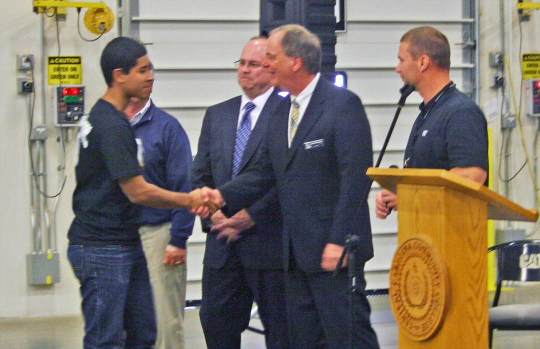 Click to enlarge,  Ellizon Torres (left), of Southern Lee High School is congratulated by CCCC President Bud Marchant (second from right) on his May 2 induction in the Caterpillar Youth Apprenticeship Program in welding. Also congratulating Torres are Donnie Oldham (behind Torres), chair of the Lee Economic Development Committee; Dr. Andy Bryan, Associate Superintendent of Lee County Schools; and Martin Kegel, facility manager for Caterpillar-Sanford. Sixteen students from Lee County public high schools were inducted into the program, which provides training for a career as a welder. The apprenticeship program is a collaboration of Caterpillar-Sanford, Central Carolina Community College, Lee County Schools, and the N.C. Department of Labor. 
