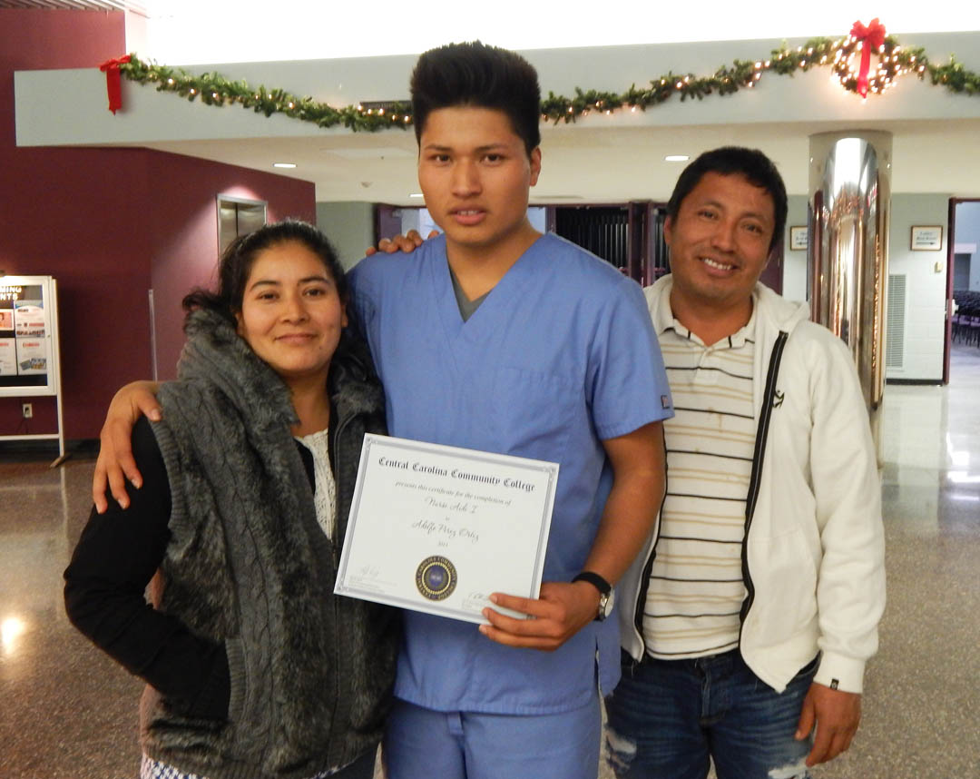 Click to enlarge,  Adolfo Perez (center), of Lillington, flanked by his proud parents, Olga Ortiz (left) and Saul Ortiz, holds the Nurse Aide I Certificate he received at the Central Carolina Community College Continuing Education Department's Medical Programs graduation Dec. 12 at the Dennis A. Wicker Civic Center. More than 400 students completed their studies for their certificates in a variety of medical programs during the fall semester. For more information about Continuing Education medical programs at CCCC, call 919-545-8044 in Chatham County, 910-814-8823 in Harnett County, or 919-777-7793 in Lee County. For information on spring Continuing Education programs, see the schedule online at www.cccc.edu/ecd/schedule/.  
