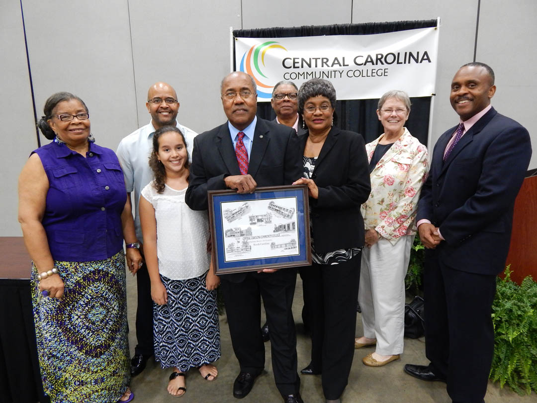 Click to enlarge,  Central Carolina Community College's Board of Trustees honored retiring member Bill Wilson Jr. at its July 23 meeting in the Dennis A. Wicker Civic Center. Wilson's friends and family gathered for the recognition. Pictured (from left, front) are Margaret Murchison, WFJA and WWGP public services director; granddaughter Lila Wilson; son Billy Wilson (back); Wilson, a CCCC trustee since 1994; Lee County Commissioner Robert Reives (back); wife, Barbara Wilson; Kate Rumely, executive director of the Brick Capital Community Development Corp.; and N.C. Rep. Robert Reives II. Wilson holds a pen-and-ink collage of college buildings by artist Jerry Miller, which was presented to him by Board of Trustees Chair Julian Philpott and CCCC President Bud Marchant. 