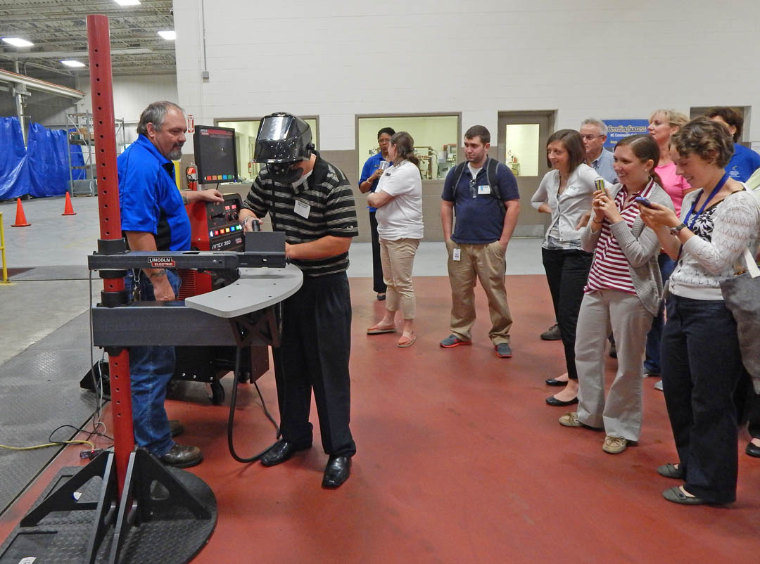 Click to enlarge,  Lee County Schools educators watch as Central Carolina Community College welding instructor Jeff Bryant (left) shows Lee Early College guidance counselor Nick Testa how to use the college Innovation Center's welding simulator. The computer-controlled simulator trains students in the basics of welding without heat or the use of expensive metal consumables. Testa was one of a group of LCS educators taking part in an Aug. 18 Manufacturing Day put on by the college's Economic and Community Development and Student Learning, Institutional Effectiveness and Grants divisions; and the Triangle South Workforce Development Board. The event included a tour of Coty, Inc., Magnetti Marelli, and the college's Innovation Center. The educators, mostly non-vocational and technical education teachers, learned about high tech modern manufacturing and how the 'soft skills' they teach, such as teamwork, following instructions, and reading for content are critical in modern manufacturing. For more information about Lee County Schools, visit www.lee.k12.nc.us. For more information about Central Carolina Community College, visit www.cccc.edu. 