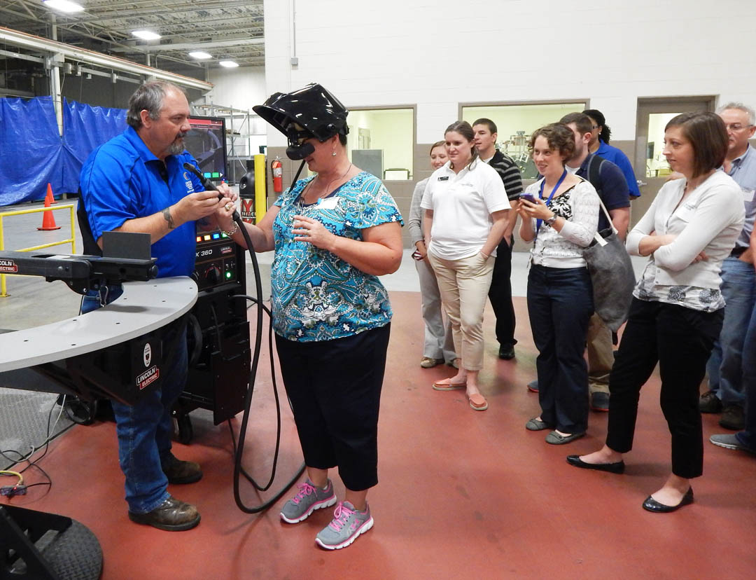Click to enlarge,  Lee County Schools educators watch as Central Carolina Community College welding instructor Jeff Bryant (left) shows Lee County High School teacher Teresa Bruner how to use the college Innovation Center's welding simulator. The computer-controlled simulator trains students in the basics of welding without heat or the use of expensive metal consumables. Bruner was one of the group of LCS educators taking part in an Aug. 18 Manufacturing Day put on by the college's Economic and Community Development and Student Learning, Institutional Effectiveness and Grants divisions; and the Triangle South Workforce Development Board. The event included a tour of Coty, Inc., Magnetti Marelli, and the college's Innovation Center. The educators, mostly non-vocational and technical education teachers, learned about high tech modern manufacturing and how the 'soft skills' they teach, such as teamwork, following instructions, and reading for content, are critical in modern manufacturing. For more information about Lee County Schools, visit www.lee.k12.nc.us. For more information about Central Carolina Community College, visit www.cccc.edu. 