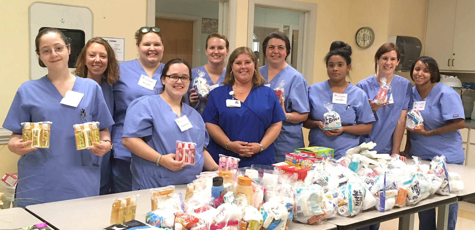 Click to enlarge,  The Central Carolina Community College Nurse Aide I night class, taught by Kim Tew, R.N., donated gift bags and supplies to Harnett Woods Nursing Home residents and staff on Aug. 2, 2017. Included in the donations were socks, lotions, body/bath soaps, combs, tissues, shampoos, and shaving cream, as well as animal crackers, peanut butter crackers, and oatmeal pies. Fifty individual bags were made for the Harnett Woods' residents. Boxes of supplies for the Dementia Unit were also donated. Over 150 pairs of socks were purchased and donations of soft cookies and muffins were donated to the Activity Room for the residents' morning coffee fellowship. Additionally, the Harnett Woods' staff was shown appreciation with candies for each nursing station. Pictured with Harnett Woods Activity Director Tonya Tart-Ellis are CCCC students Maggie Gietzen, Amber Birkner, Samantha Jacobs, Mary Craft, Savannah Matthews, Valerie Godfrey, Pacia Lindsey, Rachel Thompson, and Ebony Johnson. 