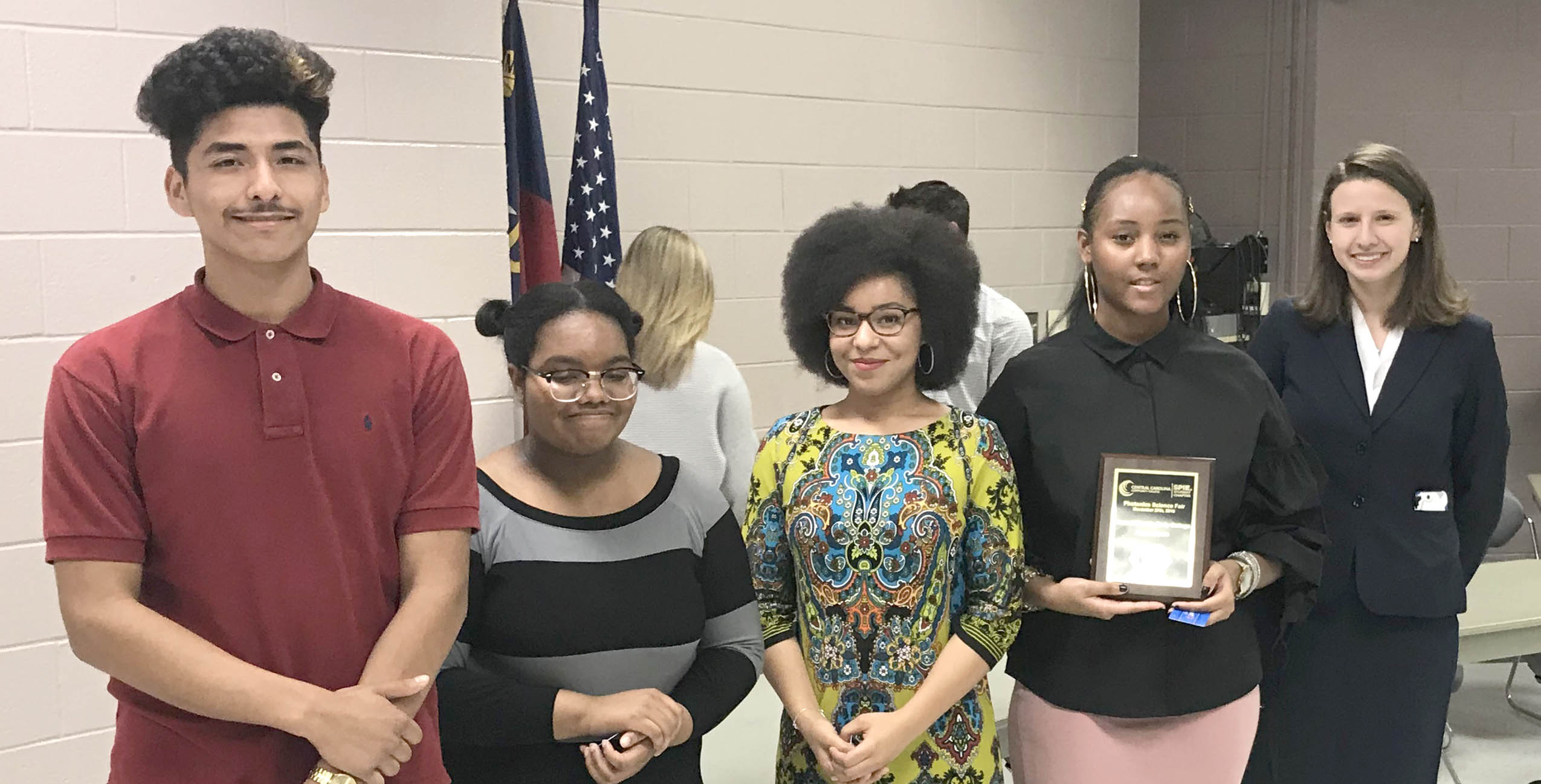 Click to enlarge,  Isabelle Karis (right), second-year CCCC laser student and Laser Club president, presents an award to members of the Harnett Early College team. 