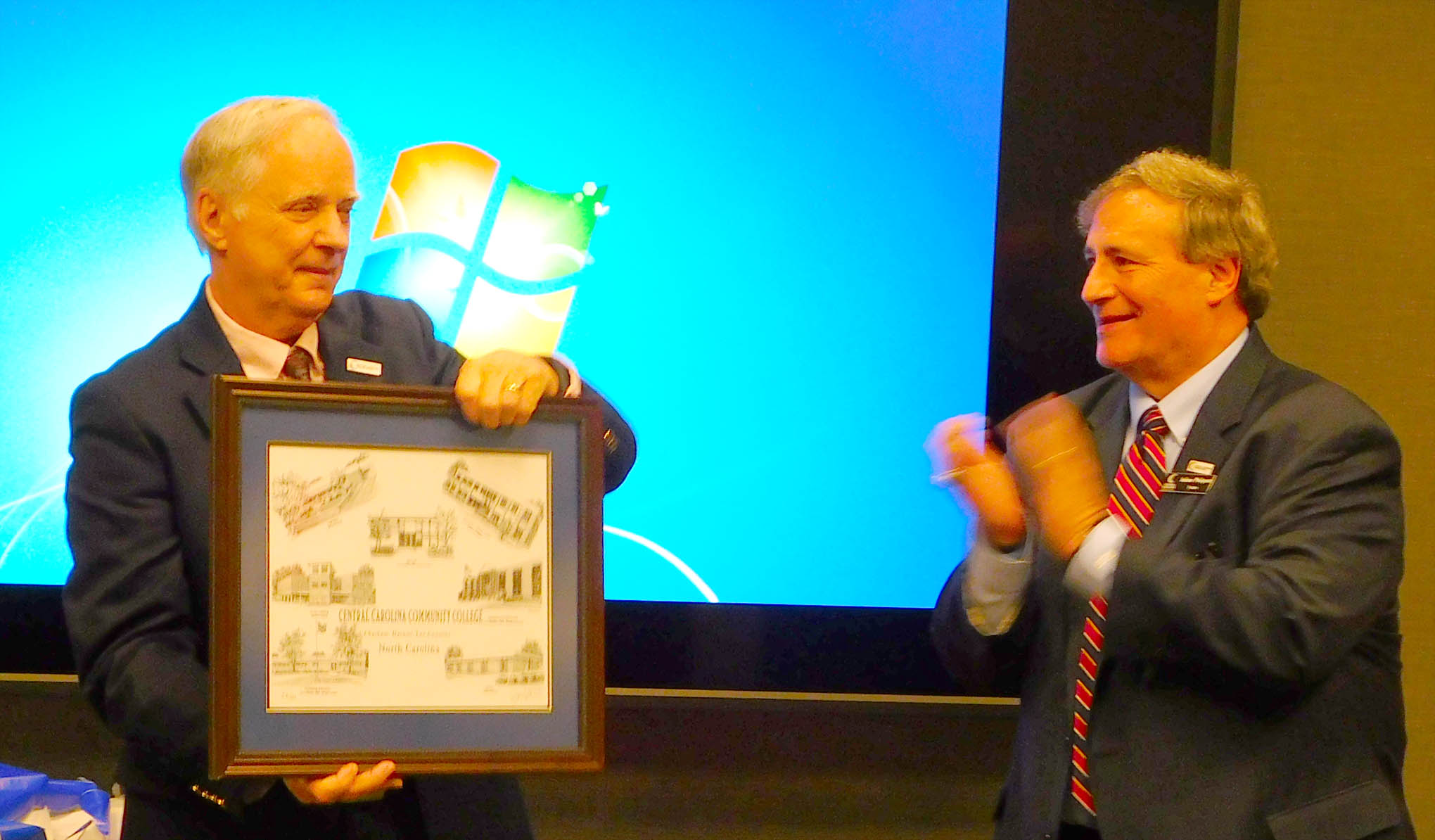 Click to enlarge,  Mark Cronmiller (left), pictured with CCCC Board of Trustees Chairman Julian Philpott (right), was presented with a Jerry Miller print of CCCC buildings, as he was honored for his service as a CCCC Trustee on Wednesday, Feb. 13.  