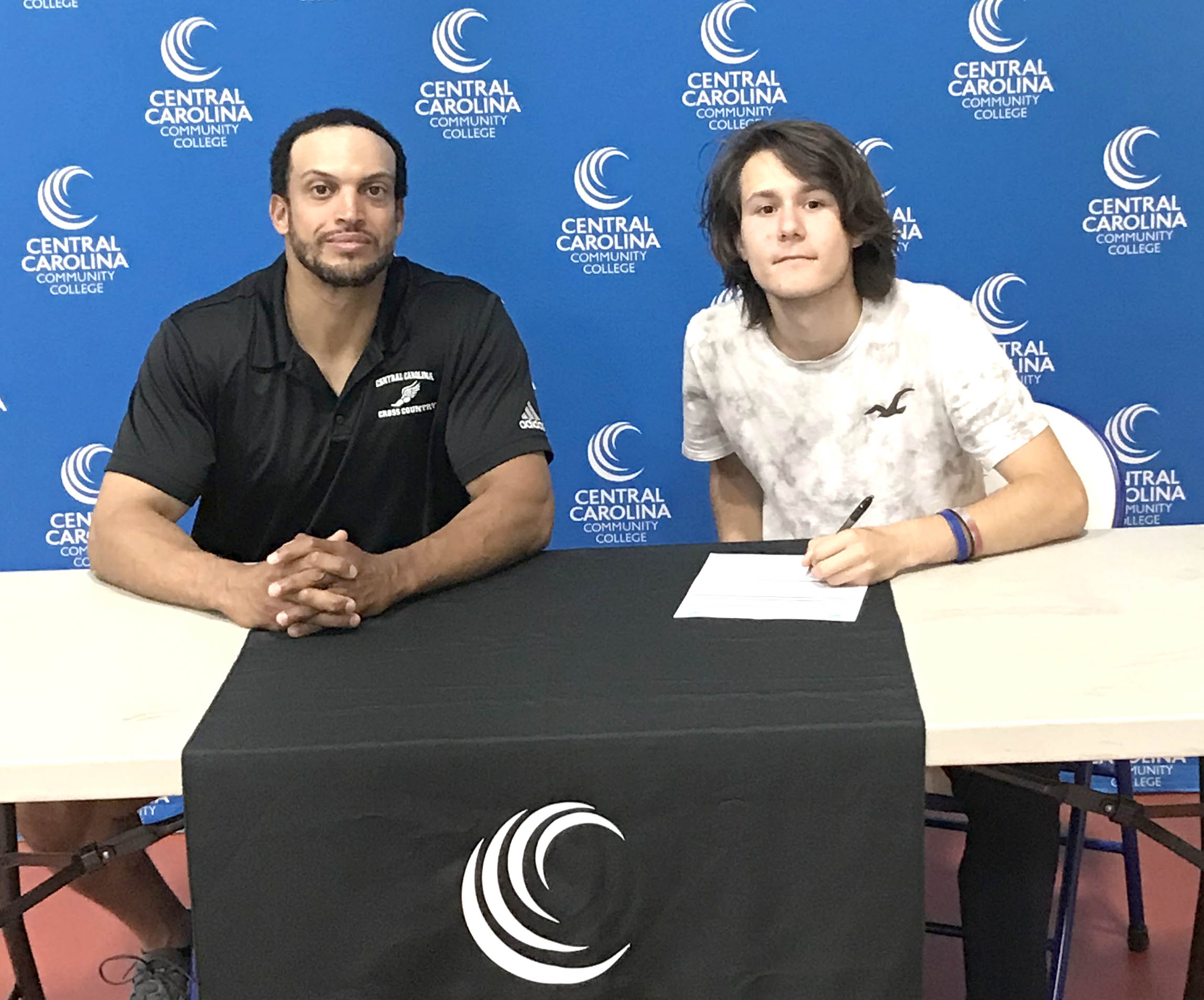 Click to enlarge,  Gavin Rankin (seated, right) signs with the Central Carolina Community College cross country program. Seated at left is CCCC Head Cross Country Coach Richard Briggs. 