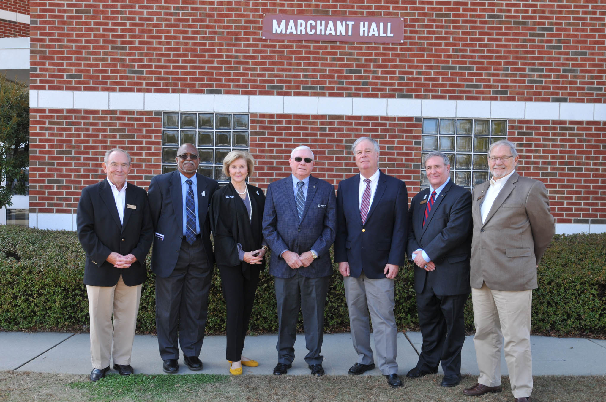 Click to enlarge,  Dr. T. Eston "Bud" Marchant (third from right) is pictured with Central Carolina Community College Trustees (left to right) Douglas "Doug" H. Wilkinson Jr., James French, Jan Hayes, L.W. "Bobby" Powell, Julian Philpott, and Bill Tatum, in front of Marchant Hall on the CCCC Lee Main Campus in Sanford, N.C. 