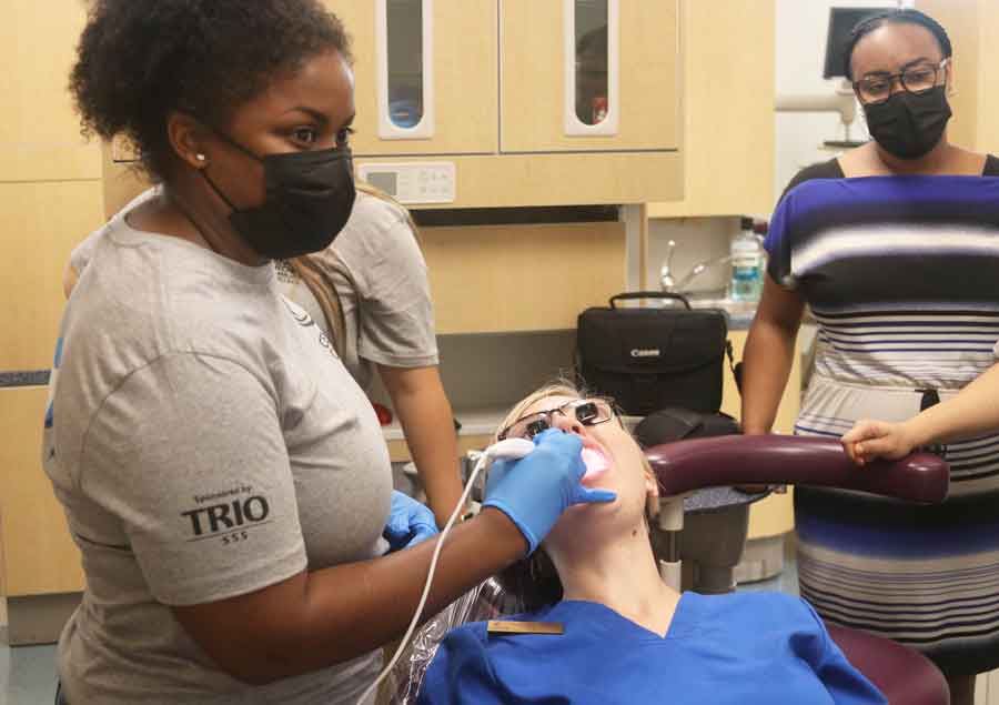 Click to enlarge,  Student Ashjamel Revels, left, gets her opportunity to try intraoral photography during the Prep for Success Academy at Central Carolina Community College, with dental hygiene clinic manager Danielle Bruner serving as patient and academic coach Ashley Mullins watching the computer screen where the images were being displayed. 