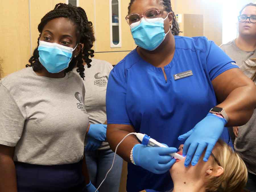 Click to enlarge,  With students Afia Sarpong, left, and LeeAnn Lilly watching the monitor, dental hygiene clinical coordinator Macy Woods demonstrates how to position the camera to get digital images that dental professionals use to treat patients. 