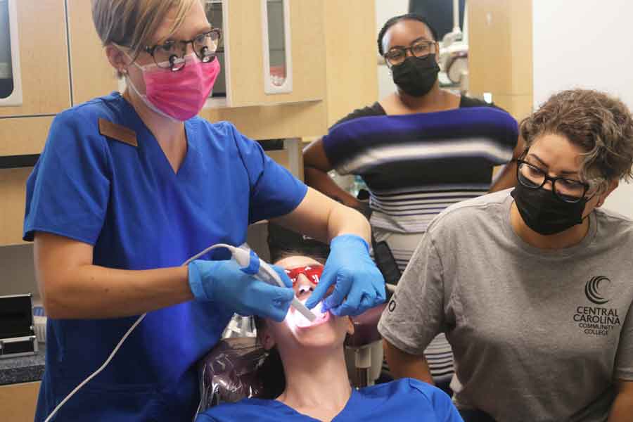 Click to enlarge,  Danielle Bruner, left, helped introduce prospective students to careers in dental assisting and dental hygiene during the four-day Prep for Success Academy. One of the hands-on demonstrations was this intraoral photography session with academic coach Ashley Mullins and student Jenny Duke, at right, watching the process unfold. 