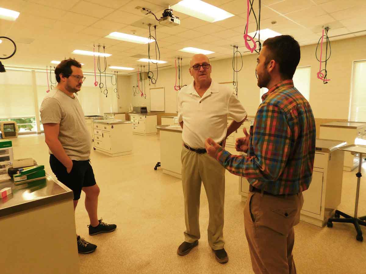 Click to enlarge,  Frank (center) and Joseph (left) Gillette visit with Justin Pedley (right), Central Carolina Community College Veterinary Medical Technology Animal Facilities Manager, at one of the VMT examination laboratories at CCCC's Dalrymple Veterinary Medical Technology Building. 